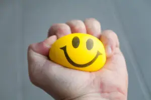 Hand squeezing yellow stress ball with smiley face