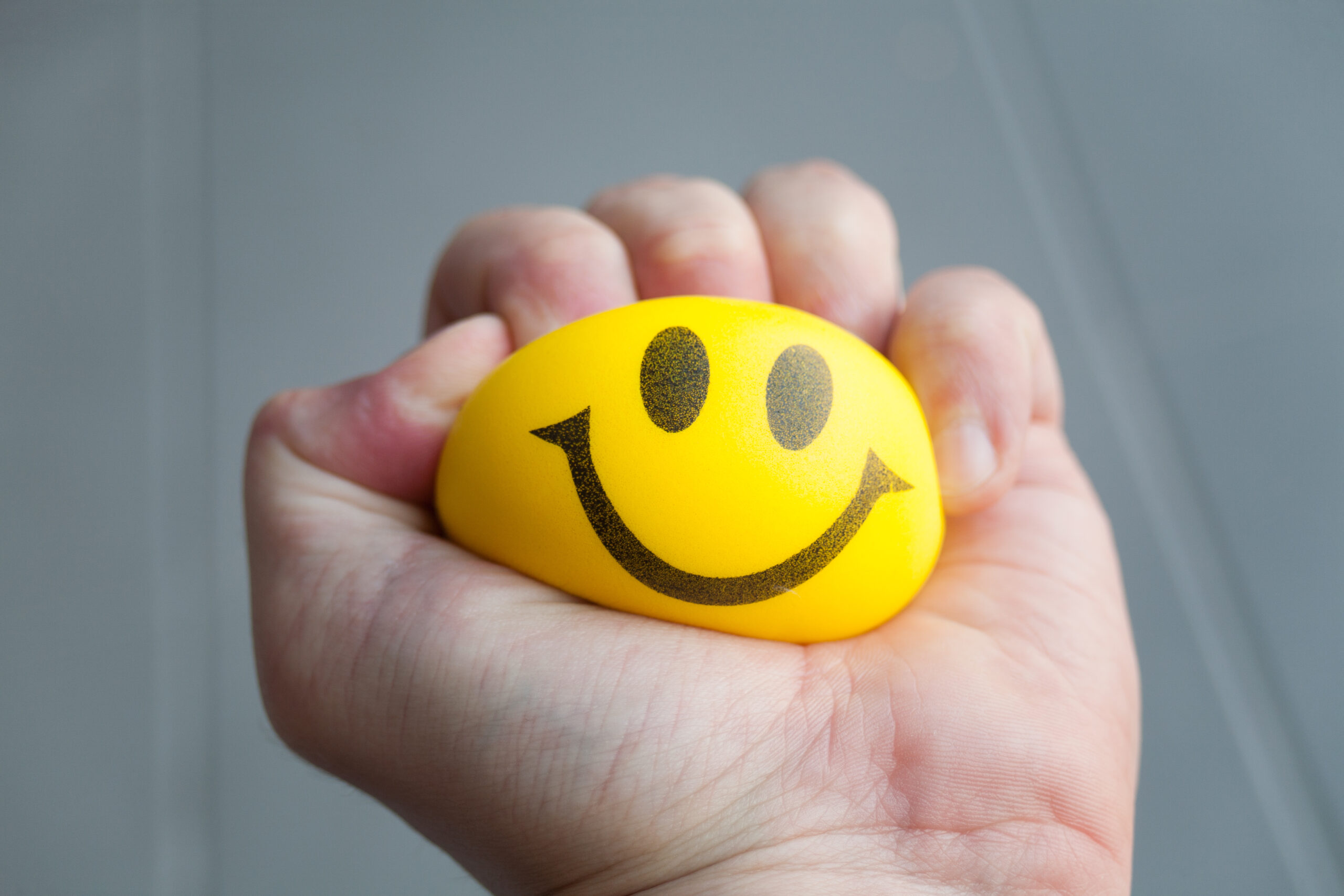 Hand squeezing yellow stress ball with smiley face